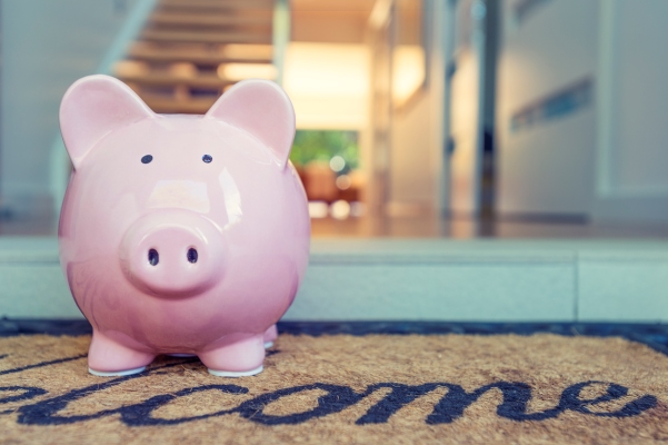 Pink piggy bank on a welcome doormat at a doorway in a home entryway.
